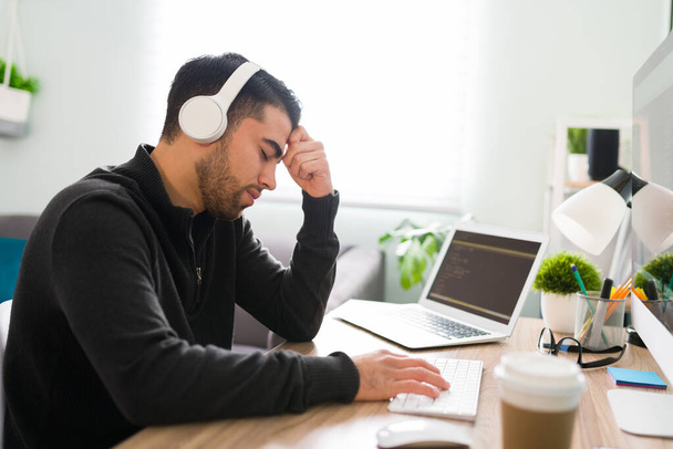 Turhautunut koodinkirjoittaja ja kehittäjä istuu toimistonsa pöydällä väsyneenä ja järkyttyneenä, koska hänen ohjelmistonsa ei toimi  - Valokuva, kuva