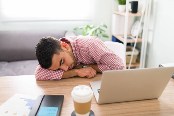 Knappe latijnse man viel in slaap tijdens het werken op zijn laptop aan zijn kantoor thuis omdat hij overwerkte - Foto, afbeelding