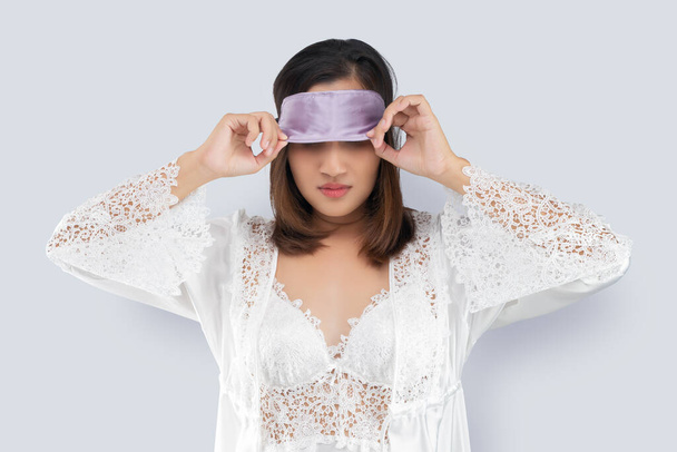 Asian woman in a lace nightgown and white satin robe take off a sleeping mask or eye mask after waking up in the morning - Photo, Image