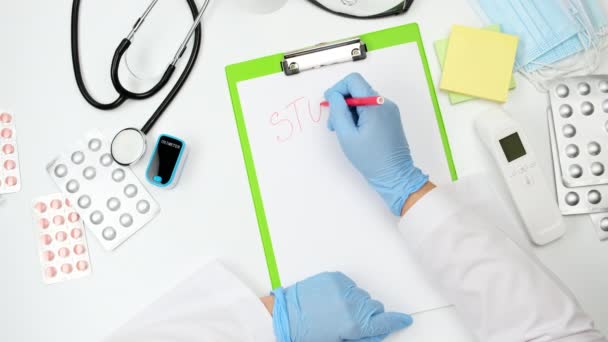 το χέρι του γιατρού σε ένα μπλε γάντι λατέξ γράφει στοπ πανικού, πάνω όψη στο γραφείο του θεραπευτή - Πλάνα, βίντεο