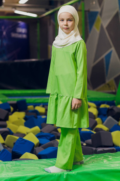 Side portrait of a little Muslim girl wearing a hijab. Concept of Muslim clothing for children. against the background of the playground. - Zdjęcie, obraz