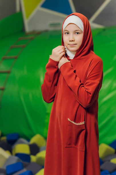 Side portrait of a little Muslim girl wearing a hijab. Concept of Muslim clothing for children. against the background of the playground. - Foto, imagen