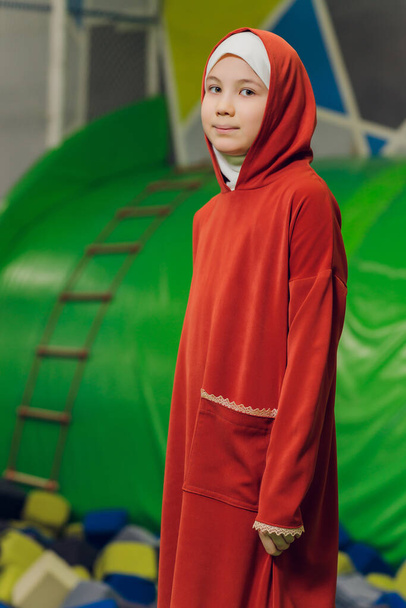 Side portrait of a little Muslim girl wearing a hijab. Concept of Muslim clothing for children. against the background of the playground. - Фото, зображення