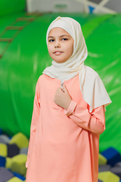 Side portrait of a little Muslim girl wearing a hijab. Concept of Muslim clothing for children. against the background of the playground. - Foto, immagini