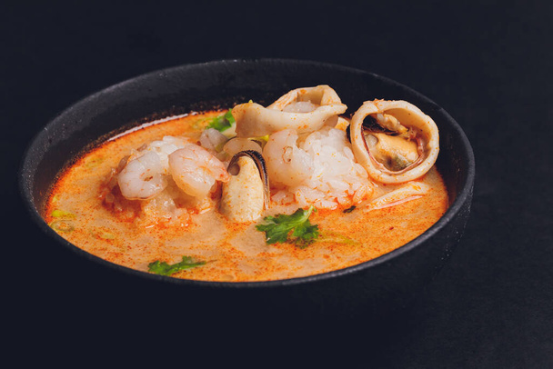 Spicy Thai soup Tom Yam with Coconut milk, Chili pepper and Seafood shrimp and salmon in a plate on a black background. Asian cuisine, restaurant menu. - Φωτογραφία, εικόνα