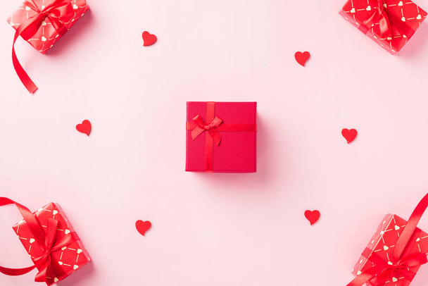 Valentines' day background. Red gift box with ribbon bow and wood red hearts shaped composition greeting card for love isolated on pink background with copy space. Top View from above - Valokuva, kuva