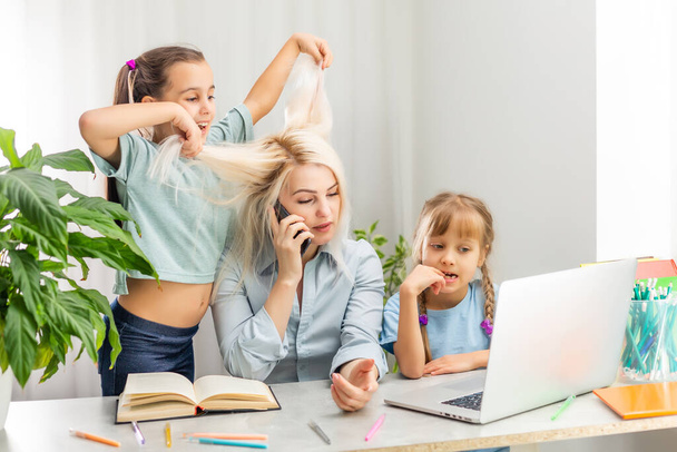 Une jeune mère avec deux enfants travaille de la maison sur un ordinateur. Fatigue Lifestyle Femme au foyer Freelance. mère fatiguée et deux petites filles - Photo, image
