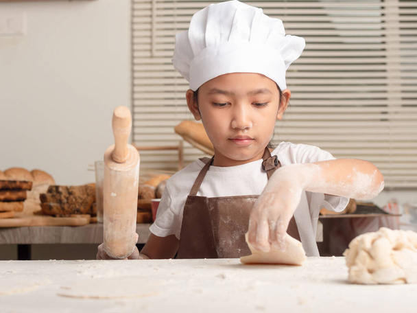 Asiática niña usando un rodillo amasando la masa en una mesa blanca para hacer panadería casera. - Foto, Imagen