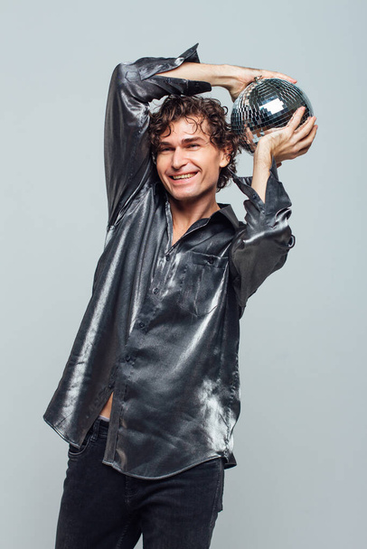 Portrait of tall attractive man with a mirror disco ball on a white background. Handsome man posing with a shiny disco ball in studio. - Foto, immagini