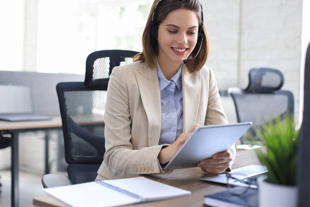 Cheerful female manager sitting at office desk and performing corporate tasks using wireless connection on digital gadgets - Photo, Image