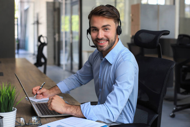 Cheerful young support phone male operator in headset, at workplace while using laptop, help service and client consulting call center concept. - Foto, Bild