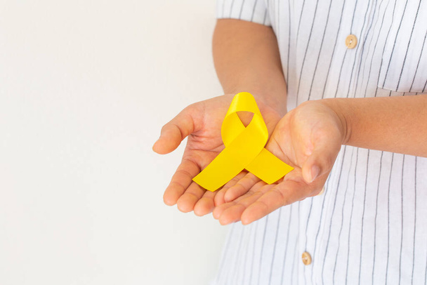 Hands holding gold ribbon on white isolated background with copy space. The international awareness symbol for Childhood Cancer. World Cancer Day. Healthcare or hospital and insurance concept. - Photo, Image