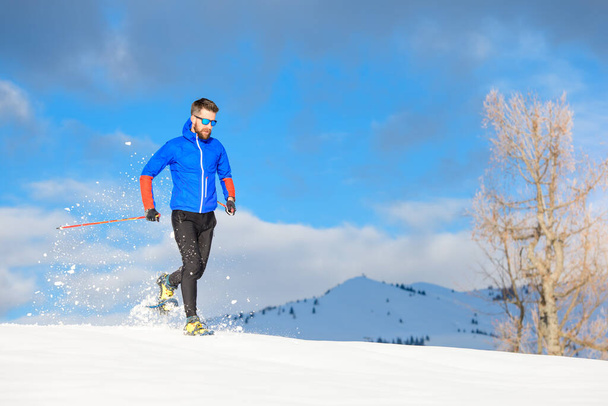 Läufer mit Schneeschuhen bergab an einem sonnigen Tag - Foto, Bild