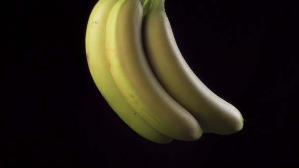 Egy csomó nem túl érett banán lóg és forog fekete háttér mellett. Közelkép - Felvétel, videó