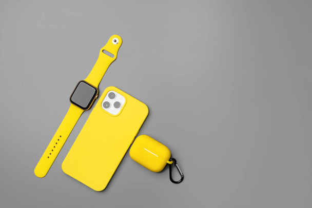Yellow smartphone, smartwatch and earphones on gray background - Fotoğraf, Görsel