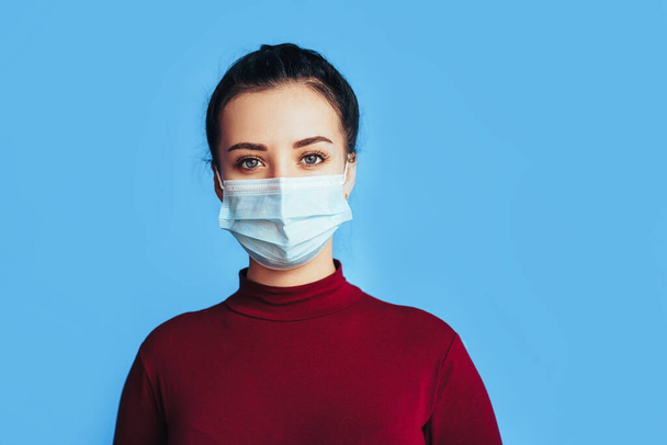 Een vrouw met een beschermend medisch masker voor een blauwe achtergrond. Gezondheidsbescherming. Preventie van ziekten tijdens een pandemie. - Foto, afbeelding