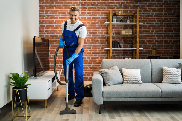 Man In Uniform Vacuuming House Floor. Cleaning Home - Foto, afbeelding