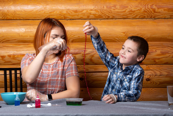 Мама і син роблять хімічні експерименти, роблячи багатокольорові полімерні черв'яки за столом удома. Навчання основ хімії в дошкільному віці - Фото, зображення