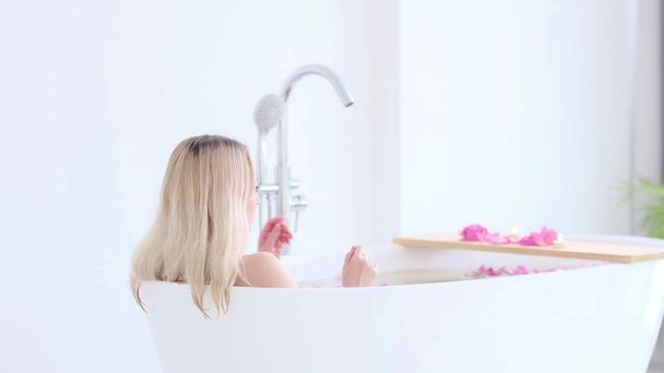 Beautiful Caucasian Blonde Girl In Bikini Lying In Flower Bath In Resort Day Spa Salon. Skin Care Therapy. Concept young woman relaxing in the bathtube. - Фото, изображение