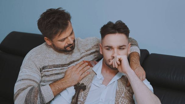 młody przystojny biały mężczyźni gej para mając problemy w związek siedzi na w kanapie i przytulanie - Zdjęcie, obraz
