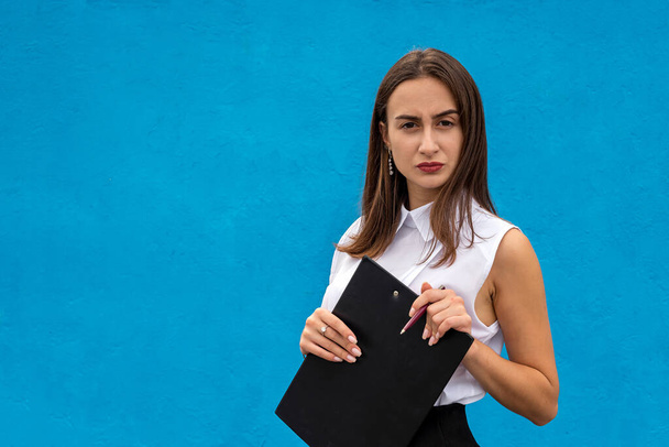 portrait of beautiful woman in business clothes with clipboard writing, isolated on blue  - Zdjęcie, obraz