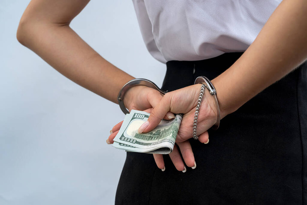 Großaufnahme von Frauenhänden in Handschellen, die Dollar halten. Bestechung und Korruption - Foto, Bild