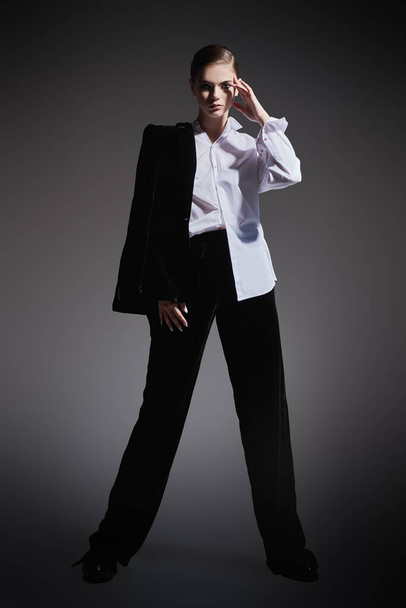Fashion concept. Full length portrait of a fashion model girl posing in black velvet suit and white shirt on a gray background.  - Foto, immagini