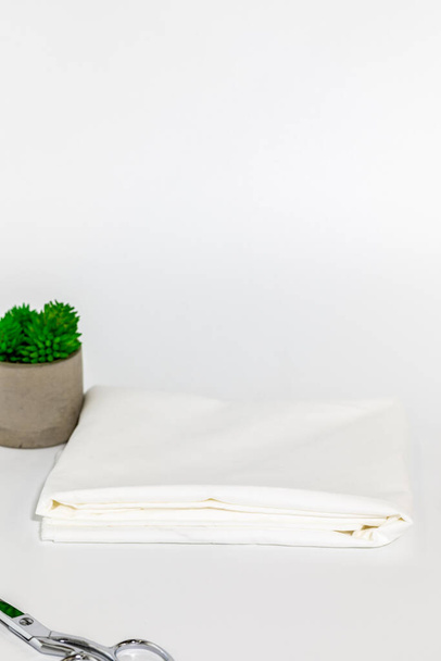 Weißer Stoff mit Schere und Zimmerpflanze auf weißem Hintergrund für Nähprojekt - Foto, Bild