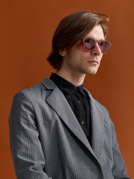 Profil-Porträt eines attraktiven, eleganten männlichen Modells mit roter Brille auf braunem Studiohintergrund. - Foto, Bild
