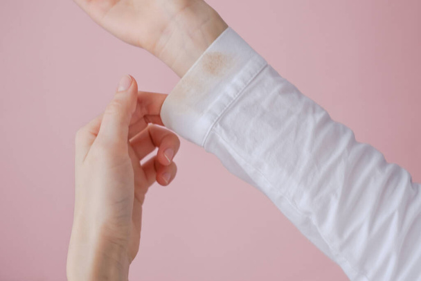 female hand showing a dirty cosmetic stain on the sleeve of a white shirt. on a pink background. High quality photo - Foto, imagen