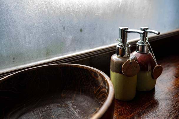 Ceramic bottles of shampoo and shower gel are placed in a large wooden bowl. And put on the wooden counter Frosted glass background Concept Thai spa for relaxation - Fotó, kép