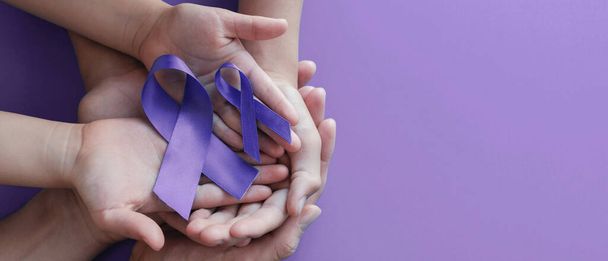 Ręce dorosłego i dziecka trzymające fioletowe wstążki, choroba Alzheimera, rak trzustki, świadomość padaczki, Światowy Dzień Raka na fioletowym tle - Zdjęcie, obraz