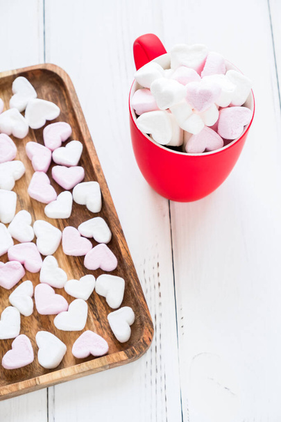 Red cup of hot cocoa with heart shaped marshmallows on white wooden background - Фото, изображение