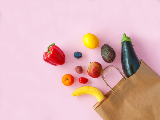 Shopping paper bag with different fruits and vegetables on a pink background, flat lay. - 写真・画像