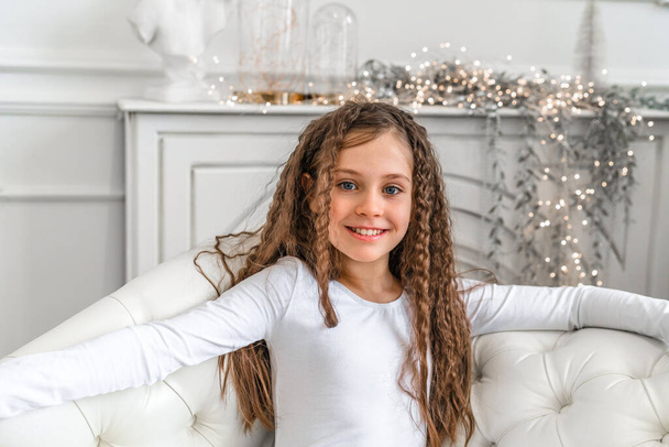 Cute little girl smiles and looks at the camera in a bright studio with Christmas decorations - Foto, Imagen