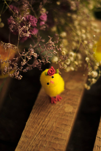 Kis húsvéti csirke virággal a fején a száraz virágok között és egy fa felületen - Fotó, kép