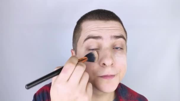 De man kijkt in het frame en gebruikt poeder. Close-up van een man die make-up op zijn gezicht doet. LGBT-gemeenschap, homo- of zelfzorgconcept. - Video