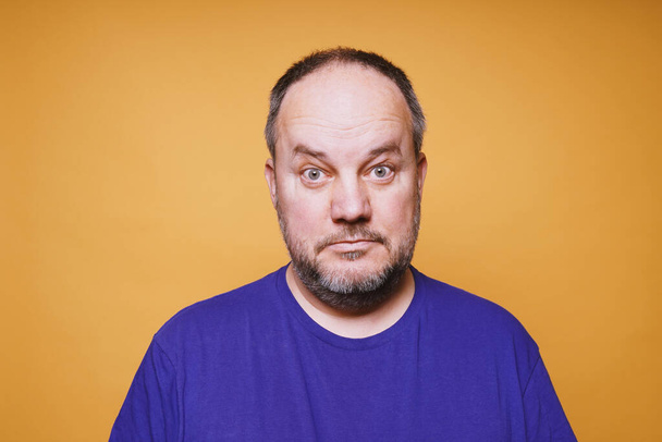 mid volwassen man met verbijsterde blik op zijn gezicht tegen oranje kleur studio achtergrond - Foto, afbeelding