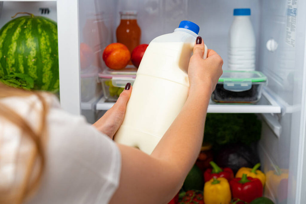 Mano femenina tomando una botella de leche de un refrigerador - Foto, Imagen