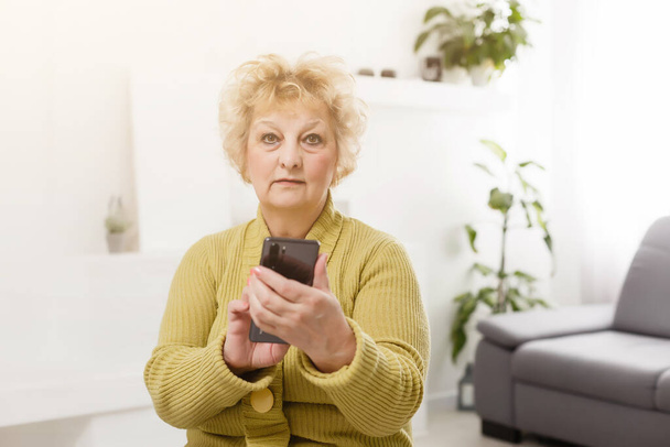 Femme âgée énervée utilisant un téléphone portable à écran tactile pour prendre des selfies ou faire un appel vidéo - Photo, image