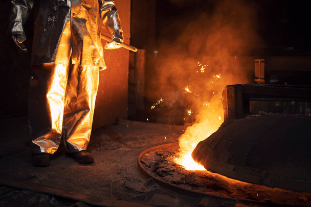 Worker in protection suit controlling iron smelting in furnace and applying heat to ore to extract a base metal. Metallurgy and heavy industry. - Photo, Image