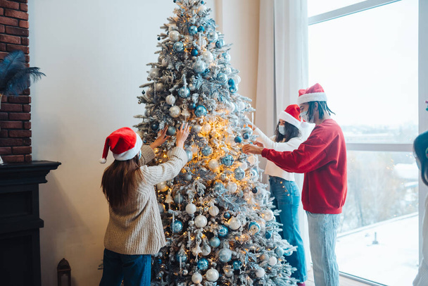 Un joven decora el árbol de Navidad con máscaras médicas. - Foto, imagen