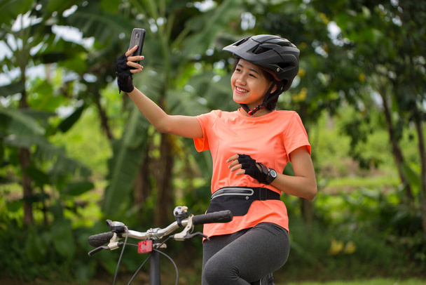 Beautiful asian woman cyclist take a self portrait with smart phone - Foto, afbeelding