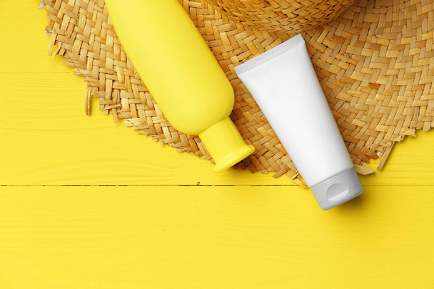 Cosmetic containers and straw hat on yellow background - Valokuva, kuva