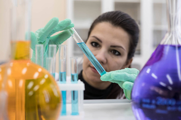Portrait of a scientist in close-up, with a test tube in his hands between chemical flasks with colored solutions. - Foto, Bild