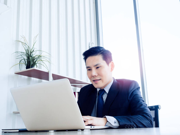 Handsome Asian businessman in suit working with laptop computer on desk inside the white office container house near glass window. Man manager using laptop in well-lit workplace. - Foto, afbeelding