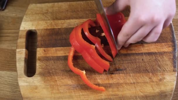 Lo chef taglia enormi peperoni rossi in cucina con un coltello affilato. Affettare il peperone dolce sul tagliere di legno. - Filmati, video