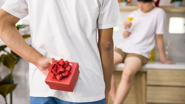 Hombre gay LGBT esconder regalo sorpresa detrás mientras su novio socio beber champán para celebrar el día de San Valentín. Asiático homosexual mismo sexo familia. - Foto, Imagen