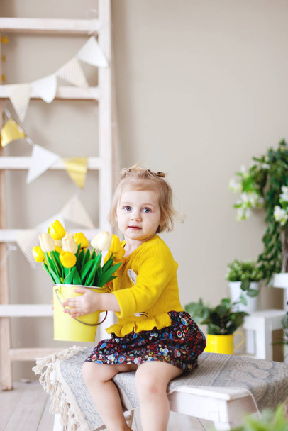 Małe dziecko w żółtej sukience z bandą żółtych tulipan.Międzynarodowy Dzień Kobiet   - Zdjęcie, obraz