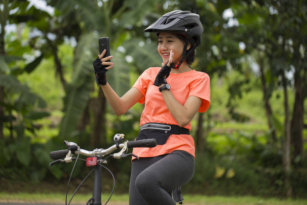 Asijské žena cyklista použití smartphone při jízdě na kole na město les. - Fotografie, Obrázek